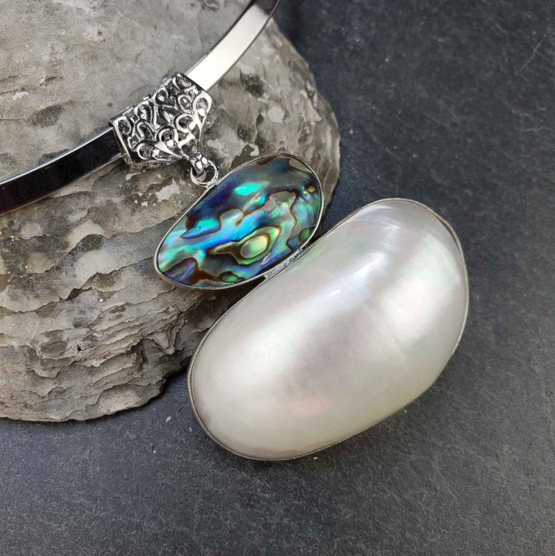 Detail van witte parelmoeren ketting met abaloon hanger aan zilveren spang liggend op steen | White Shell Green Abalone