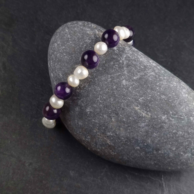 Zoetwater parel armband met witte parels en paarse edelsteen amethist liggend tegen kei | Pearl Amethyst