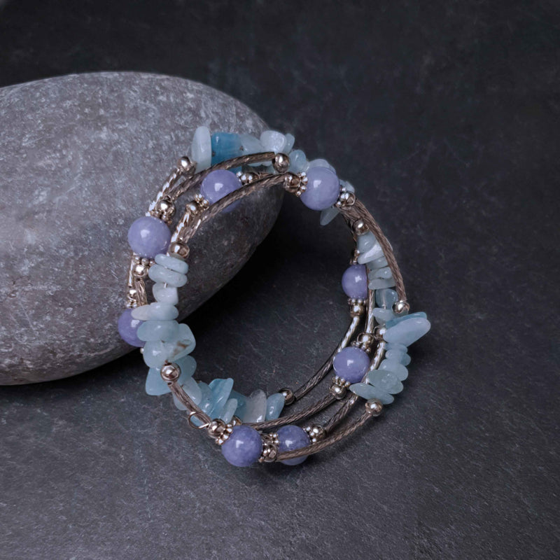 Blauw edelstenen wikkelarmband met aquamarijn en aventurien liggend tegen steen, vooraanzicht | Four Loops Blue Gemstone