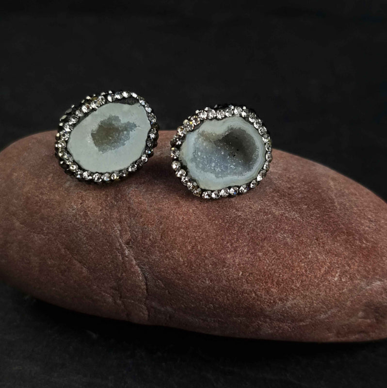 Licht grijze edelstenen oorknoppen met ijskwarts en stras steentjes liggend op rode kei | Bright Natural Ice Quartz