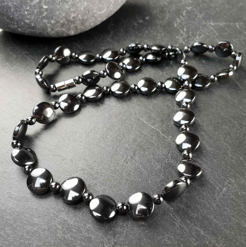 Zwarte edelstenen ketting met magneetslot en hematiet stenen liggen op grijze steen | set Hematite Coin