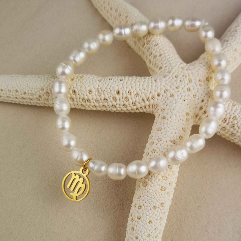 Wit zoetwater parel armband met goud edelstalen bedeltje van sterrenbeeld Maagd liggend op zeester en zand | Gouden Sterrenbeeld Maagd