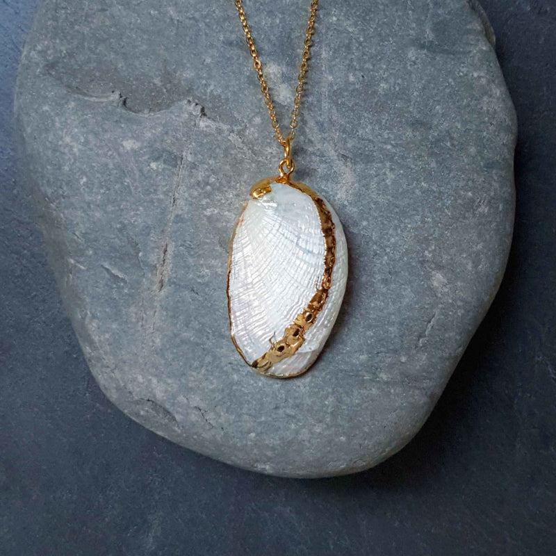 Parelmoeren schelpen ketting met witte schelp aan gouden ketting liggend op kei | White Shell Gold
