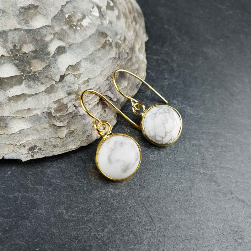 Witte edelstenen oorbellen met howliet en goud edelstaal liggend tegen schelp| Howlite Gold Round