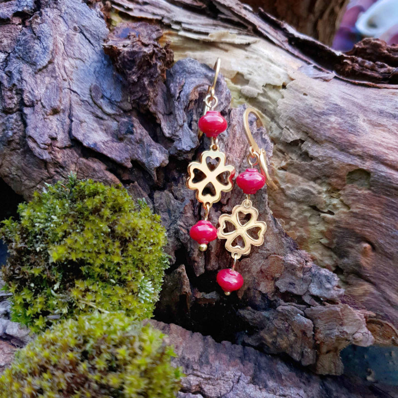 Rood koralen oorringen met goud klavertje vier van edelstaal liggend op hout | Lucky