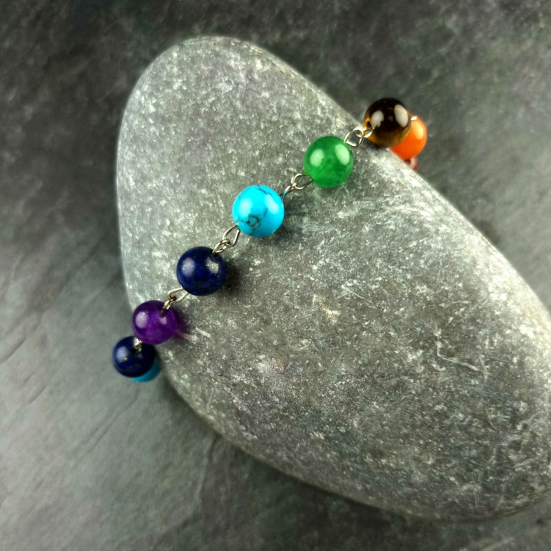 Edelstenen armband met veel gekleurde edelstenen| regenboog armband | Chakra armband liggend op kei | Gemma