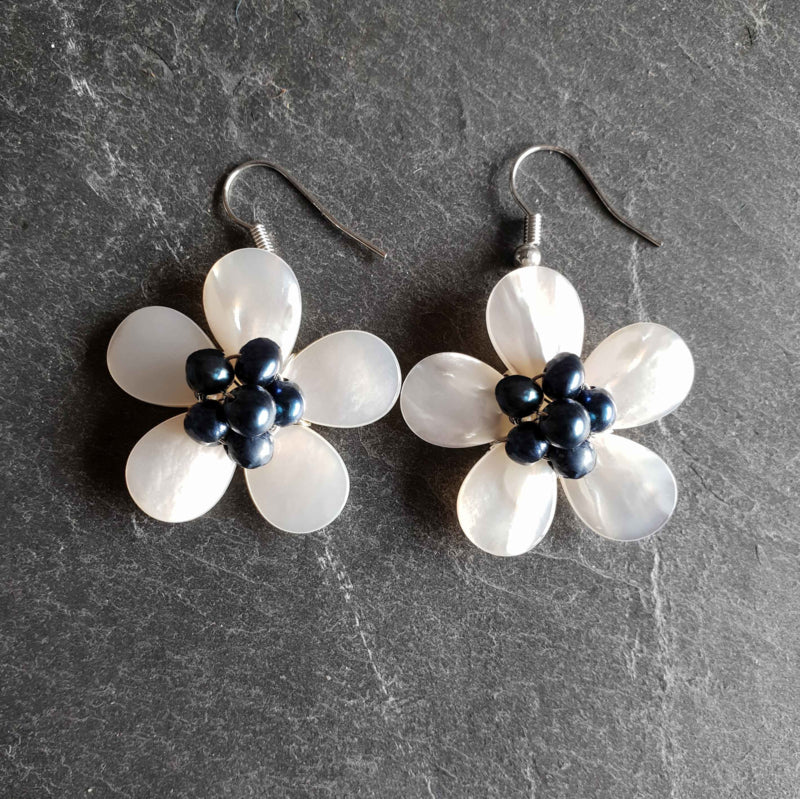 Zoetwater parel oorbellen met blauwe parels en wit parelmoer in bloem vorm met zilver edelstaal liggend op leisteen | White Shell Flower Blue Pearl