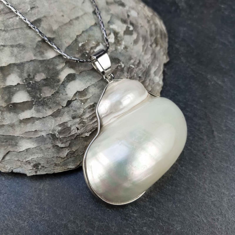 Witte schelpen ketting met zilver edelstaal liggend op leisteen | set Pearl White Turbo Shell