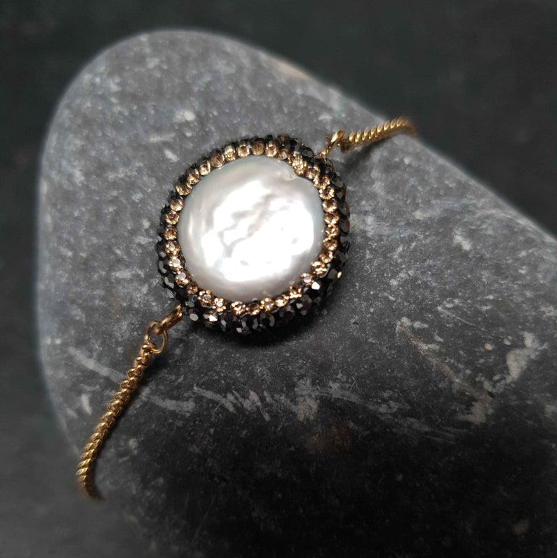 Wit zoetwater parel armband met goud edelstaal, stras steentjes en een schuifslotje liggend op kei | Bright Minimal Gold Coin