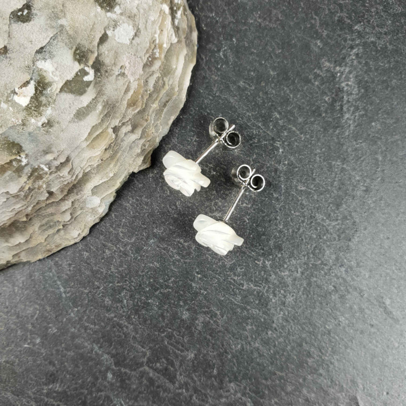 Witte parelmoeren oorknopjes in bloem vorm liggend op leisteen bovenaanzicht | White Shell Flower 8 mm