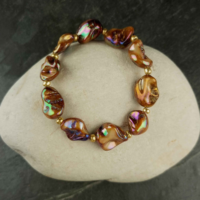 Bruin parelmoeren schelpen armband met goud edelstaal liggend op witte kei | set Shell AB Brown Gold