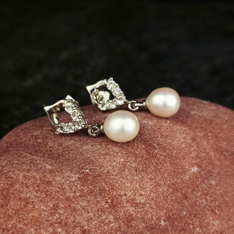 Witte zoetwater parel oorbellen met stras steentjes liggend op rode steen | Bling Pearl Heart W