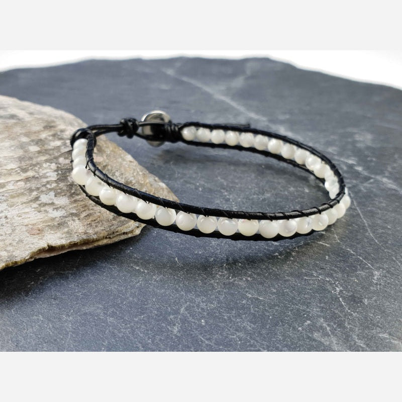 Parelmoeren armband met wit parelmoer en zwart leer liggend tegen schelp | White Shell Wrap