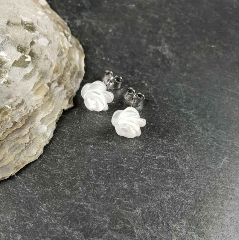 Witte parelmoeren oorknopjes in bloem vorm liggend op leisteen | White Shell Flower 8 mm