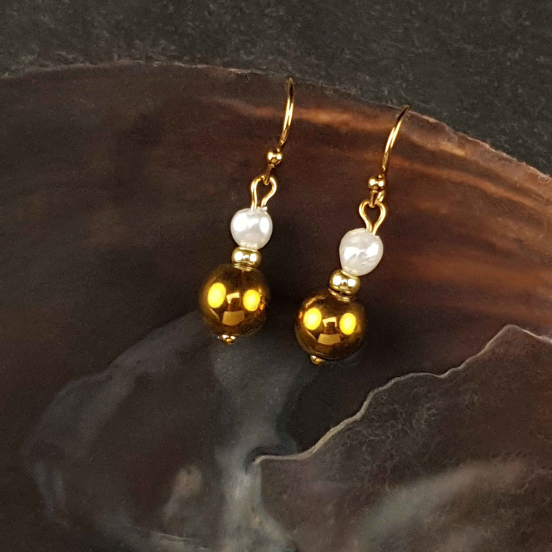 Witte zoetwater parel oorbellen met goud edelstaal en goud hematiet liggend in schelp | Bold Gold Pearl Hematite