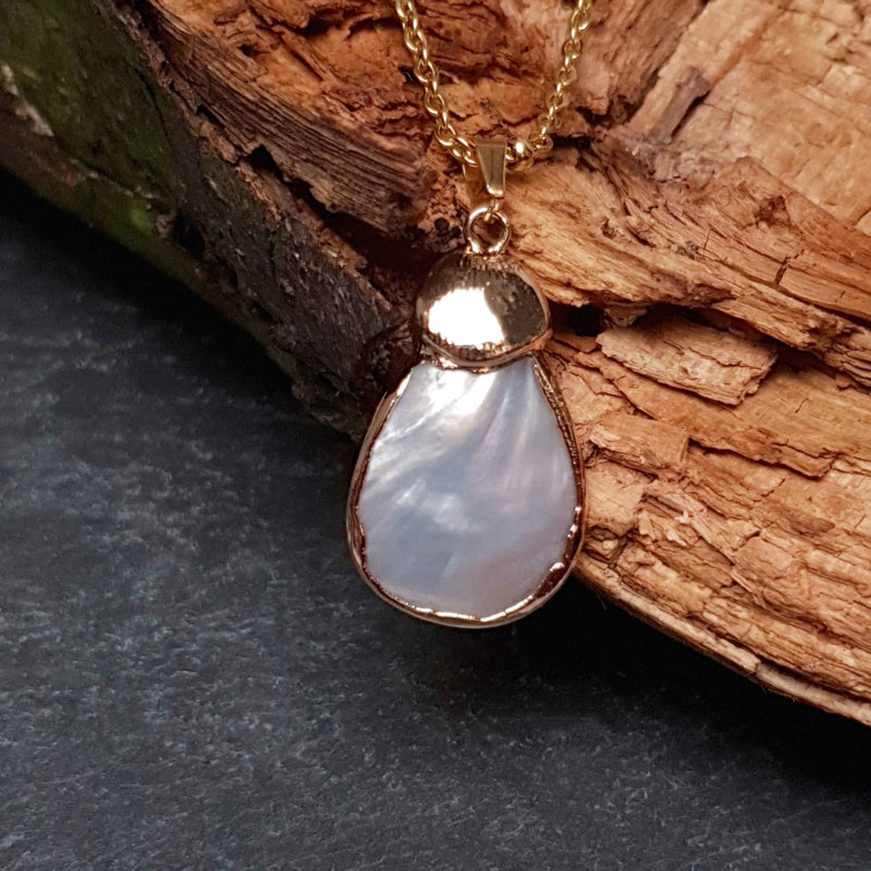Detail van witte parelmoeren ketting met wit parelmoer hanger aan gouden edelstalen ketting hangend aan hout vooraanzicht | Gold Shell