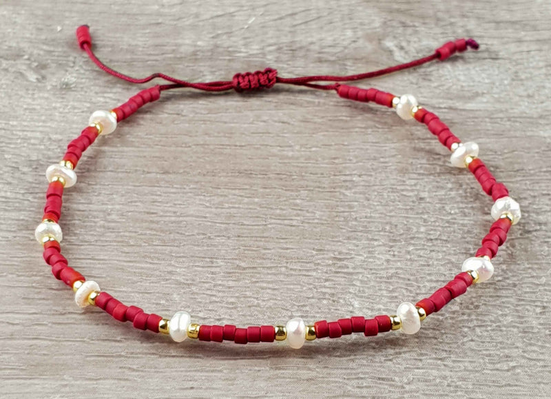 Wit zoetwater parel armband met rode en gouden kraaltjes en schuifsluiting liggend op hout | Mini Pearl Bead Red