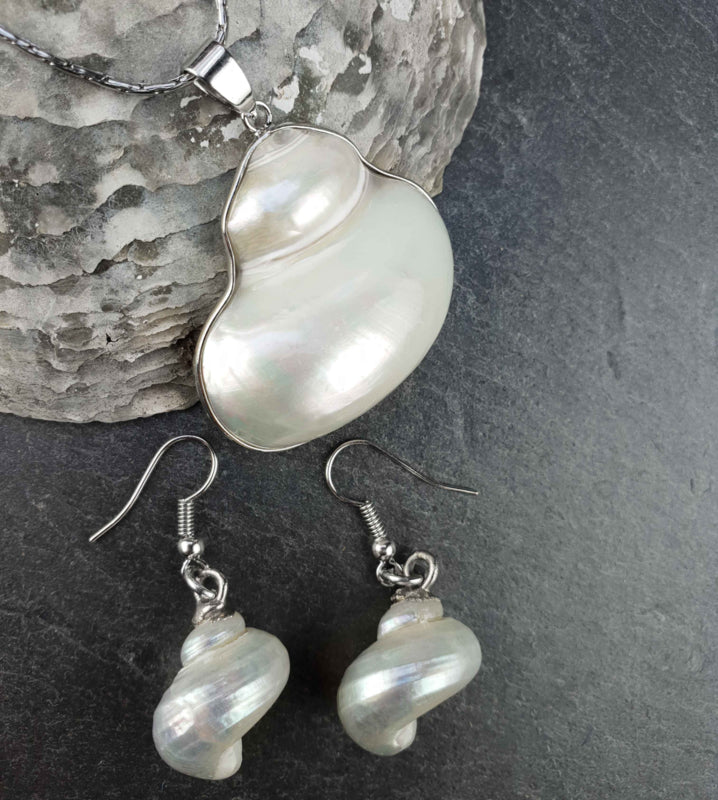 Witte parelmoeren schelpen set bestaande uit een schelpen ketting en schelpen oorbellen met zilver edelstaal liggend op leisteen | set Pearl White Turbo Shell