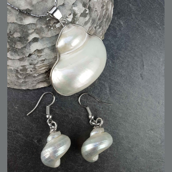 Witte parelmoeren schelpen set bestaande uit een schelpen ketting en schelpen oorbellen met zilver edelstaal liggend op leisteen | set Pearl White Turbo Shell