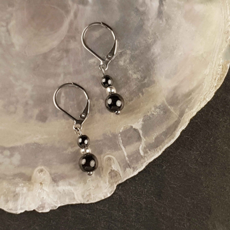 Zwarte edelstenen oorbellen met hematiet en zilver edelstaal liggend op witte schelp | Double Hematite Silver