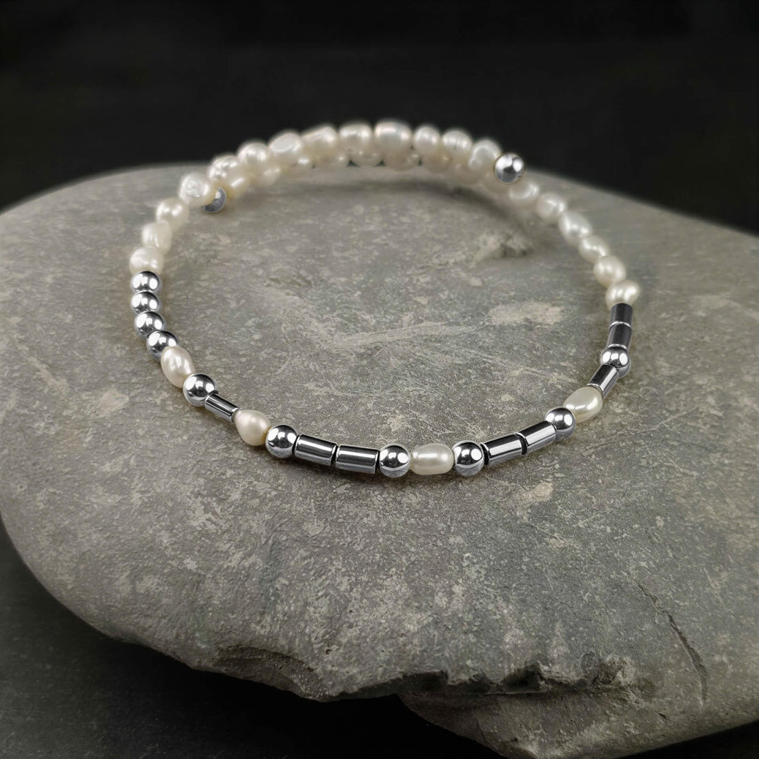 Wit zoetwater parel wikkelarmband met verbogen boodschap HAPPY in Morse code van zilveren edelstenen liggend op kei | Cadeau set zoetwater parel armband Morse Code Happy Pearl Silver