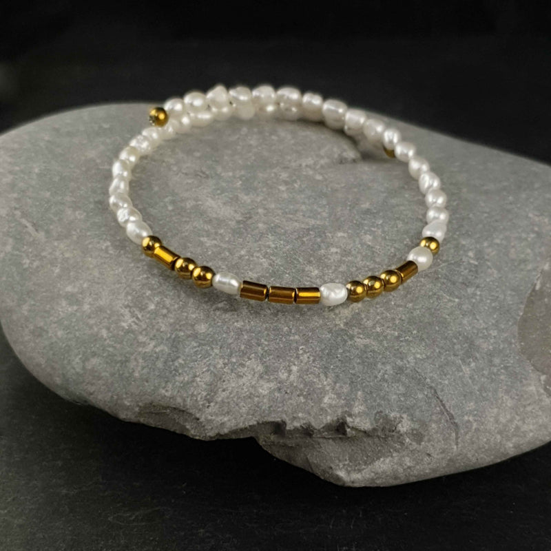 Wit zoetwater parel wikkelarmband met verborgen boodschap LOVE in Morse code met edelsteen goud hematiet liggend op kei | Cadeau set zoetwater parel armband Morse Code LOVE Pearl Gold