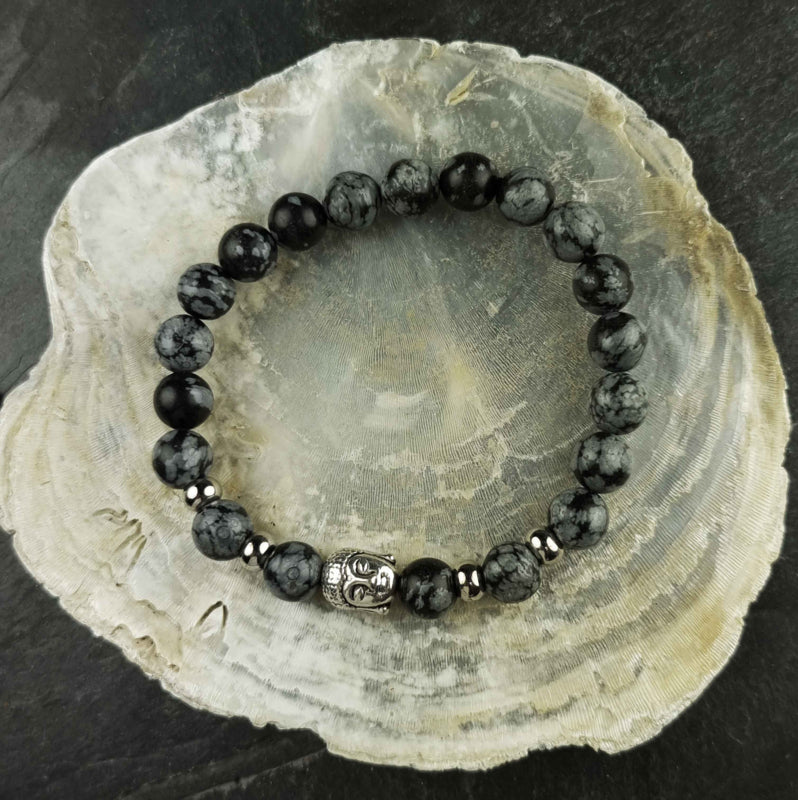 Edelstenen armband met zwart grijze edelsteen en zilver kleurige Boeddha | Elastisch liggend op witte schelp | Buddha Snowflake Obsidian