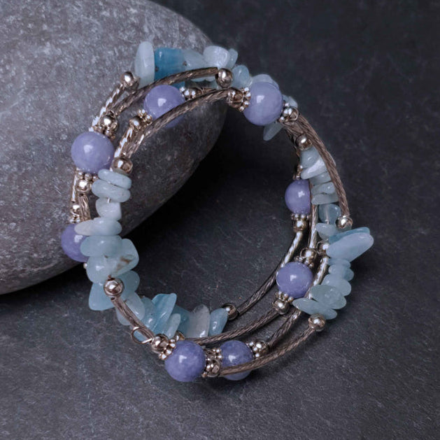 Blauw edelstenen wikkelarmband met aquamarijn en aventurien liggend tegen steen, vooraanzicht | Four Loops Blue Gemstone