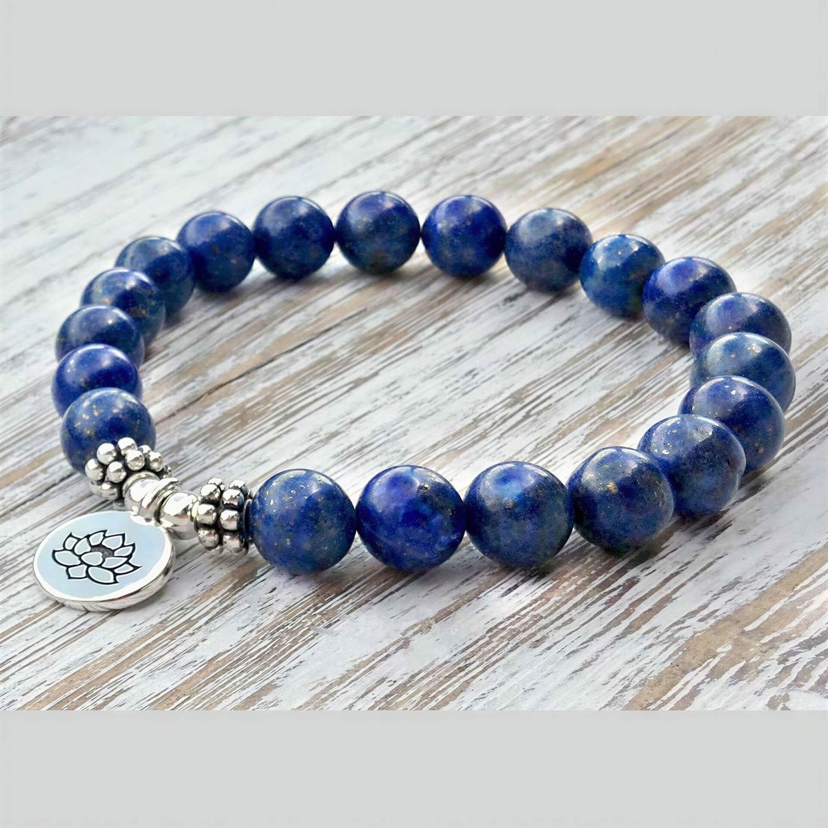 Blauw edelstenen armband met zilver lotus bedeltje, lapis lazuli armband liggend op hout