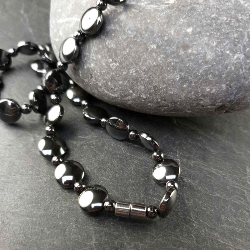 Magneetslot van zwarte edelstenen ketting met hematiet liggend op leisteen | Hematiet Coin