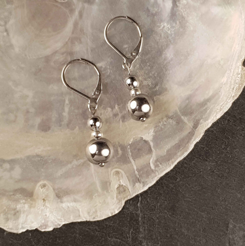 Edelstenen oorbellen met zilver hematiet en edelstaal liggend op witte schelp| Bold Silver Hematite