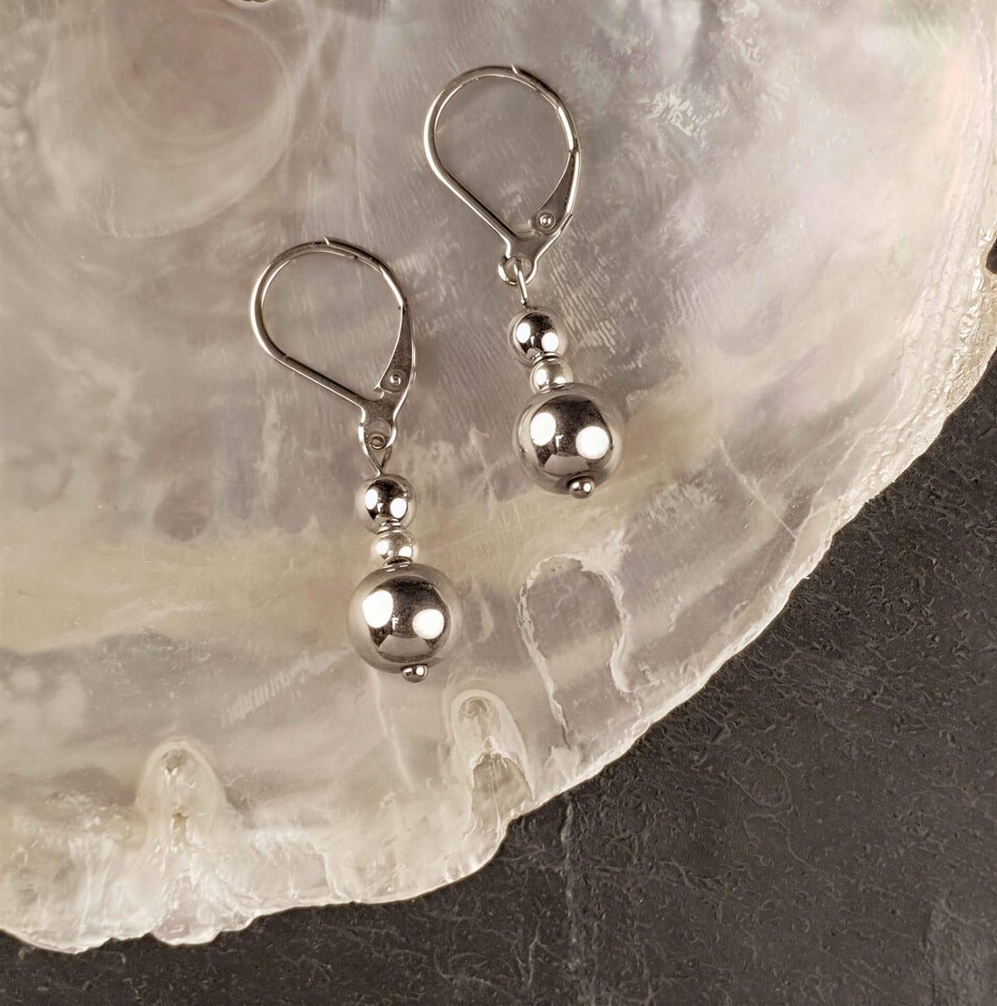 Edelstenen oorbellen met zilver hematiet en edelstaal liggend op witte schelp| Bold Silver Hematite