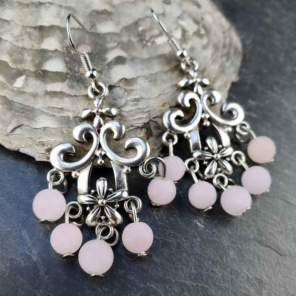 Lange roze edelstenen oorbellen met rozenkwarts en sterling zilver (925) liggend tegen schelp | Chandelier Frozen Rosé Quartz