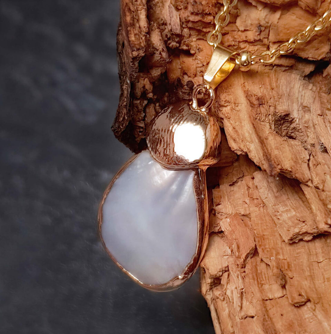 Detail van witte parelmoeren ketting met wit parelmoer hanger aan gouden edelstalen ketting hangend aan hout | Gold Shell