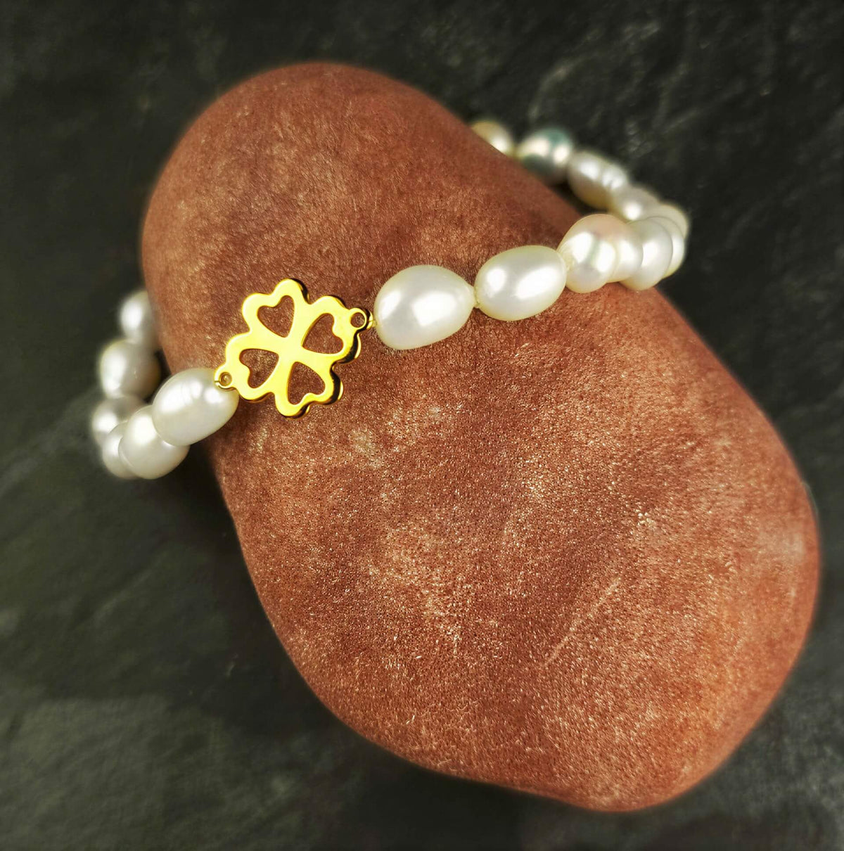 Wit zoetwater parel armband met een klavertje 4 van goud edelstaal liggend op rode steen | Good Luck Groot Klavertjje 4 Goud