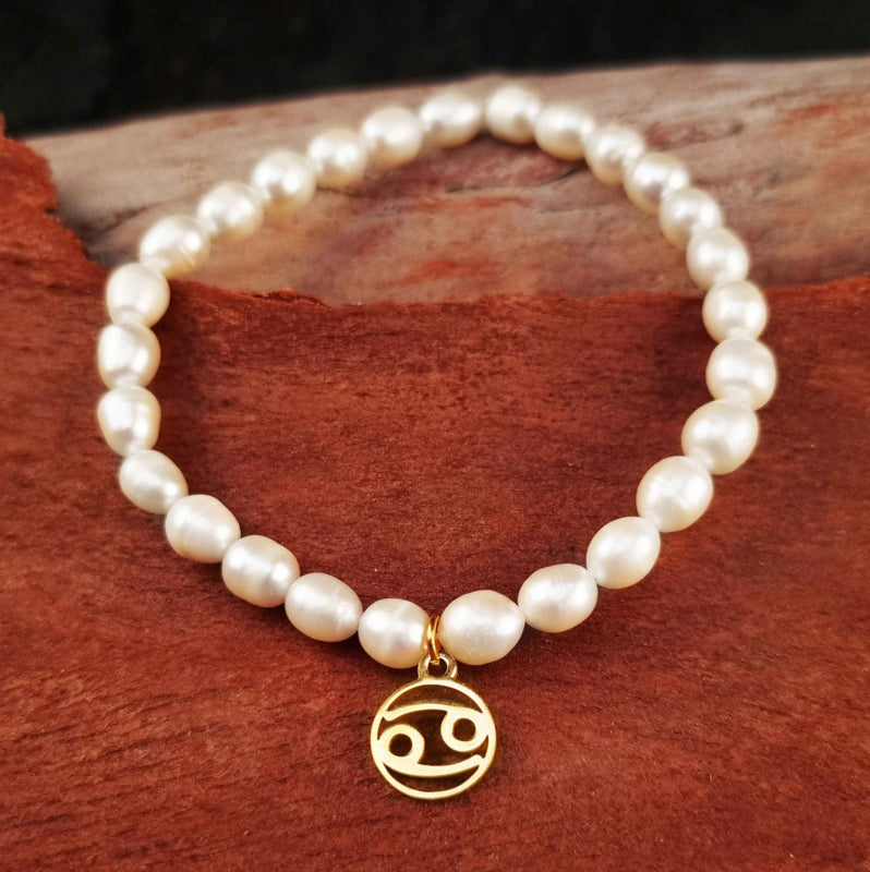 Wit zoetwater parel armband met goud edelstalen bedeltje van sterrenbeeld Kreeft liggend op hout | Gouden Sterrenbeeld Kreeft