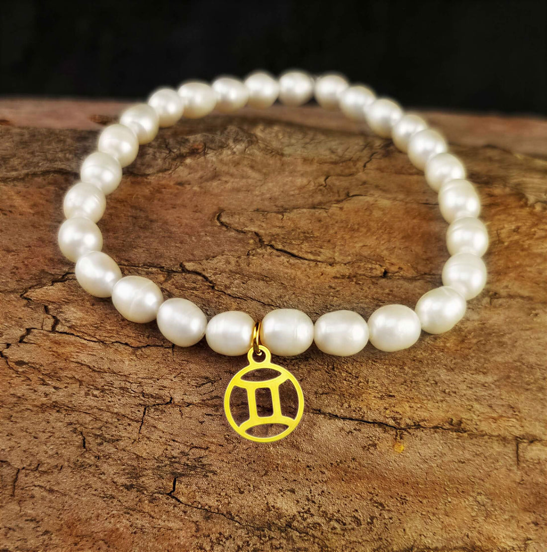 Wit zoetwater parel armband met goud edelstalen bedeltje van sterrenbeeld Tweeling liggend op hout | Gouden Sterrenbeeld Tweeling