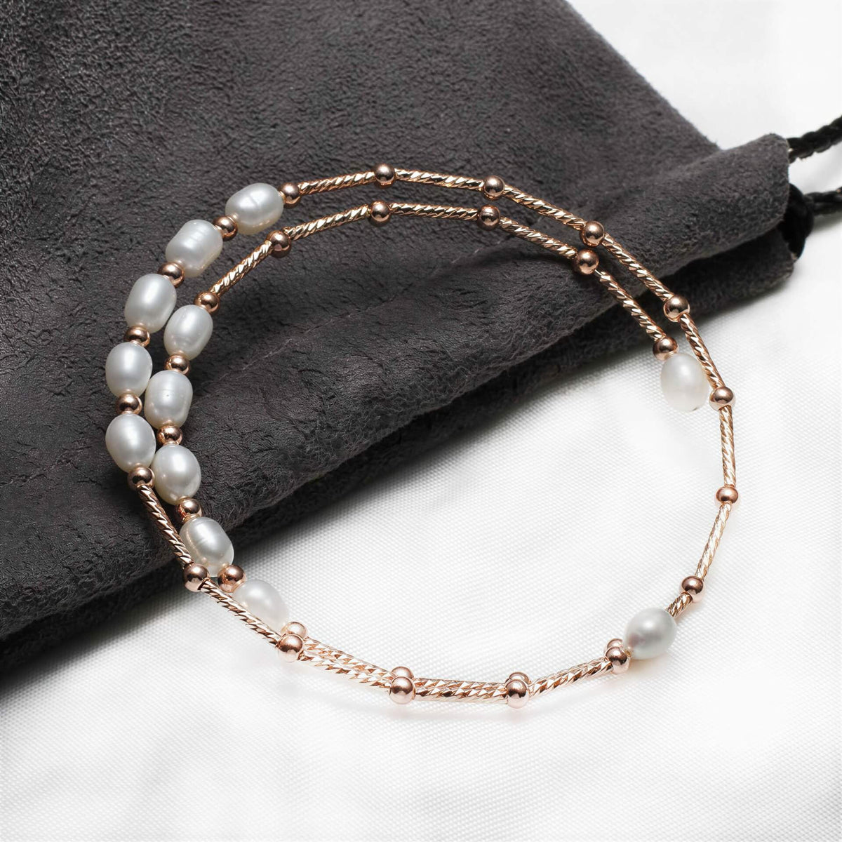 Zoetwater parel wikkel armband met witte parels en rose goud liggend op zakje | Wrap Rose White Pearl