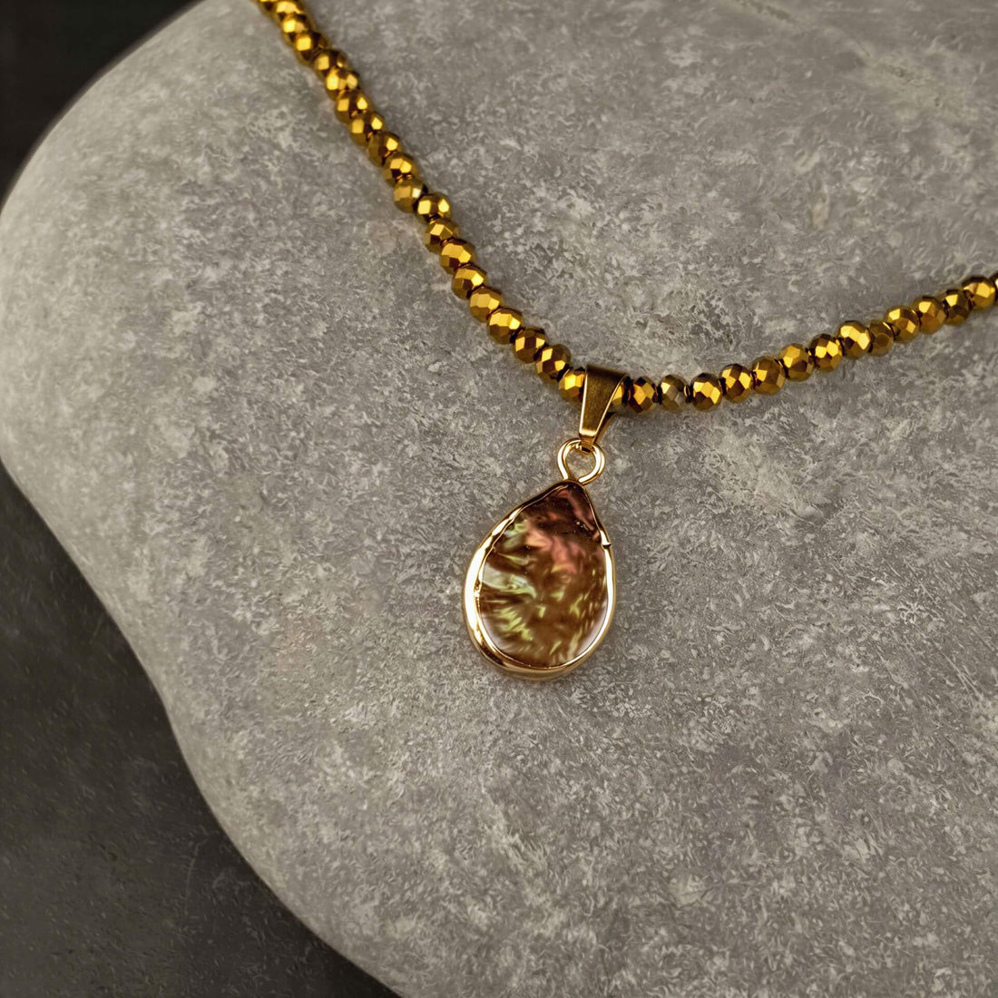 Zoetwater parelketting met bruine parel hanger, goud facet geslepen glaskristallen en goud edelstaal liggend op kei | Badia