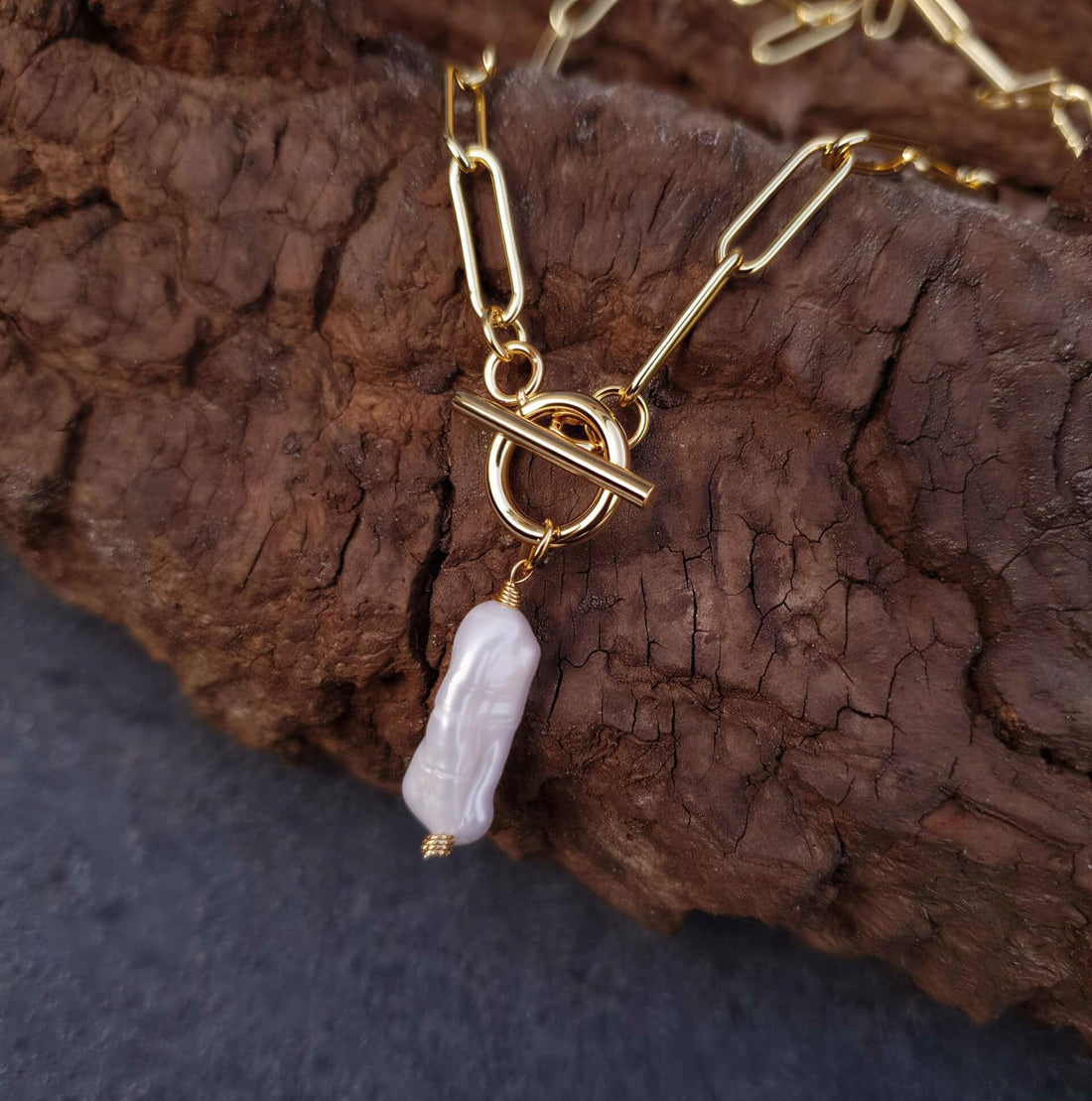 Zoetwater parelketting met witte parel hanger aan goud edelstalen paperclip ketting liggend op hout | Biwa Pearl Gold Paperclip