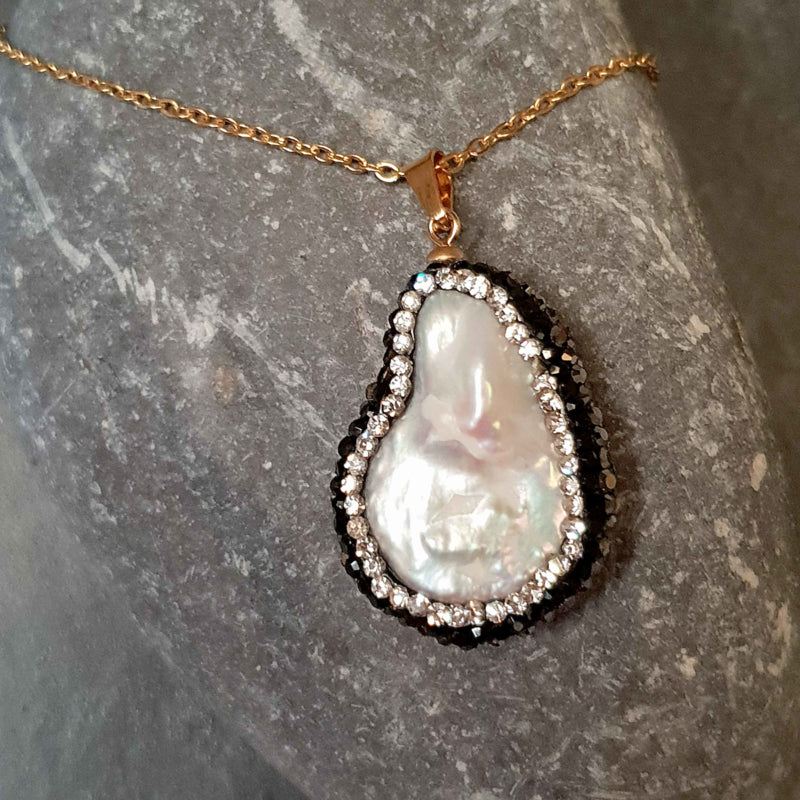 Detail van zoetwater parelketting met witte parelhanger met gouden en zwarte stras steentjes en goud edelstaal liggend op kei | Bright Minimal Gold Teardrop