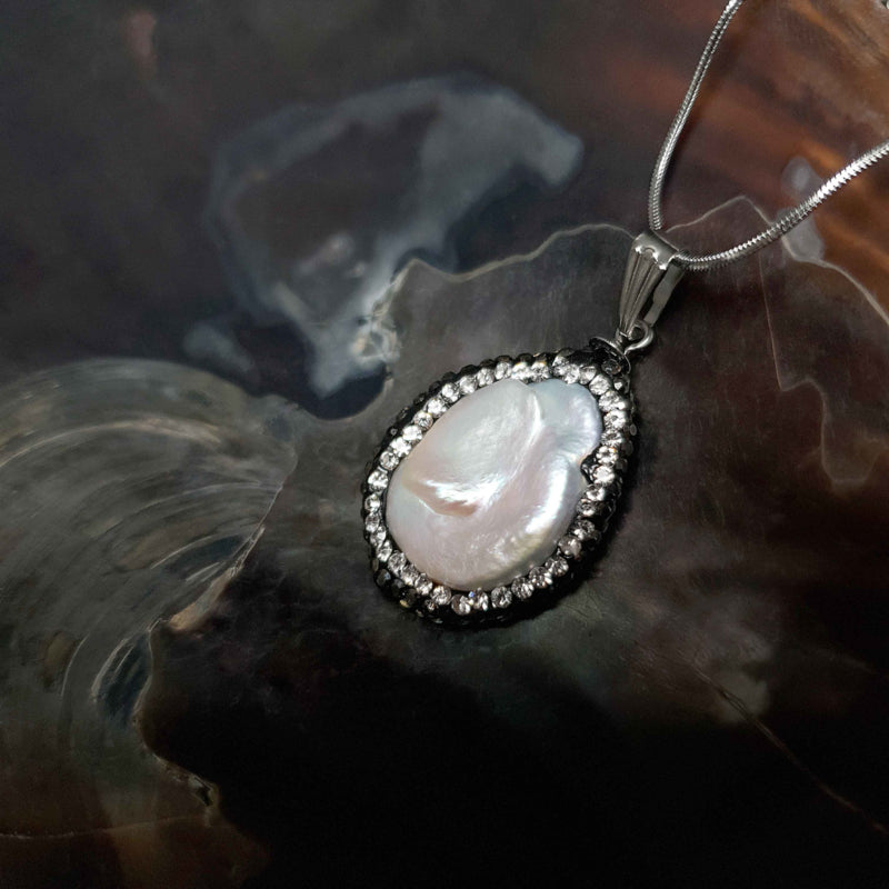 Detail van zoetwater parelketting met witte parel hanger met stras steentjes en zilver edelstaal liggend in schelp | Bright Minimal Silver Teardrop