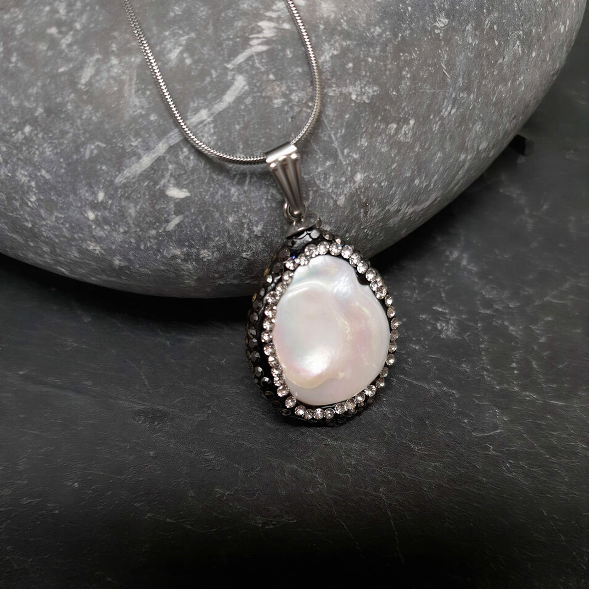 Detail van zoetwater parelketting met witte parel hanger met stras steentjes en zilver edelstaal liggend op kei | Bright Minimal Silver Teardrop