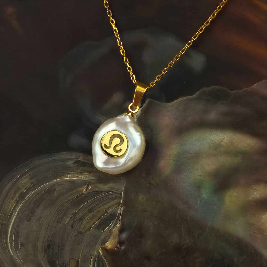 Detail van zoetwater parelketting met witte parel hanger met gouden symbool van sterrenbeeld leeuw en goud edelstaal liggend in schelp | Gouden Sterrenbeeld Leeuw