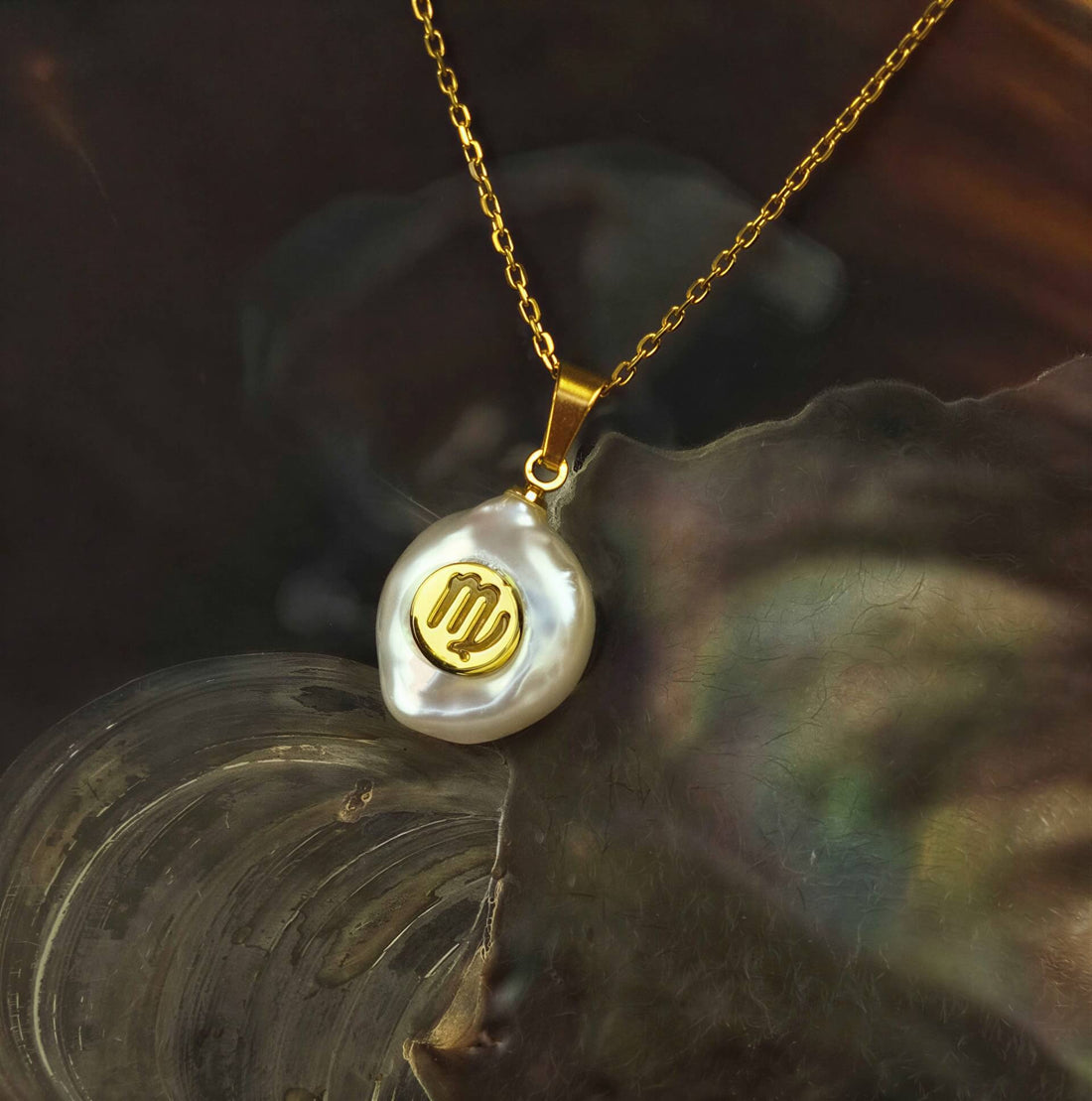 Detail van zoetwater parelketting met witte parel hanger met gouden symbool van sterrenbeeld maagd en goud edelstaal liggend in schelp | Gouden Sterrenbeeld Maagd