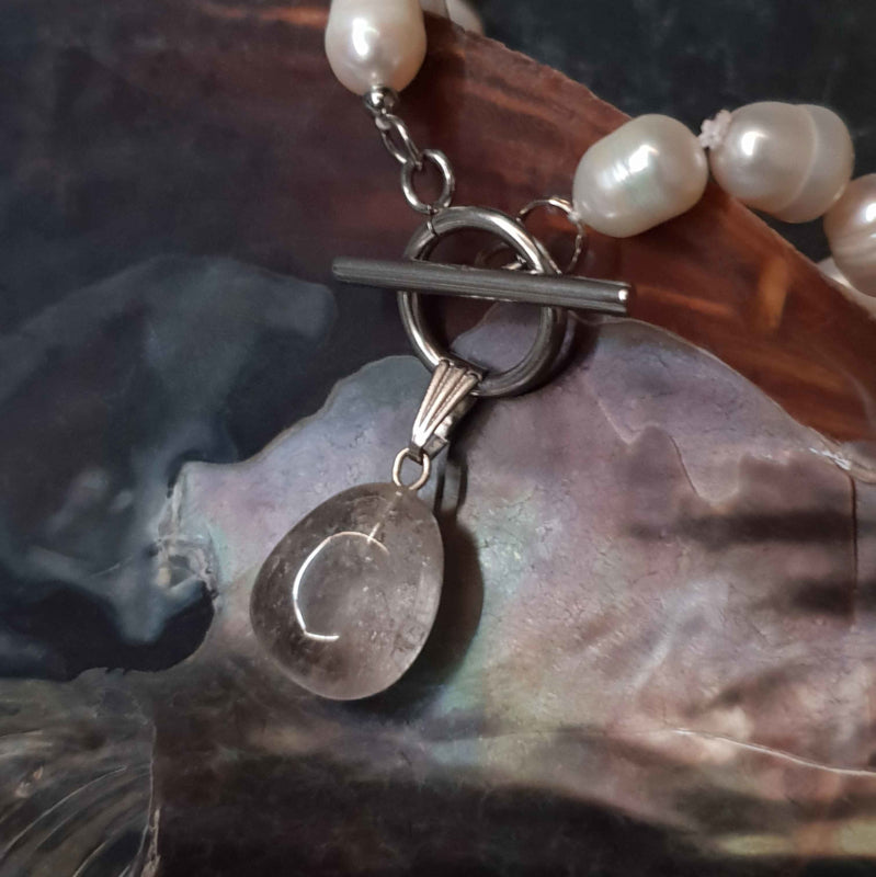 Detail van handgeknoopte zoetwater parelketting met witte parels, zilver edelstaal en rook kwarts hanger liggend in schelp | Toggle Pearl Smokey Quartz