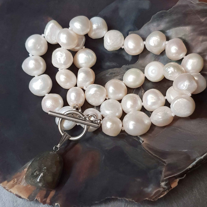 Witte zoetwater parelketting met labradoriet hanger en zilver edelstaal schuin liggend in schelp | Toggle Big Pearl Labradorite