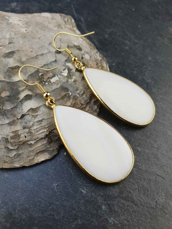 Witte parelmoeren oorbellen met goud edelstaal liggend tegen schelp | Big Taerdrop White Shell Gold