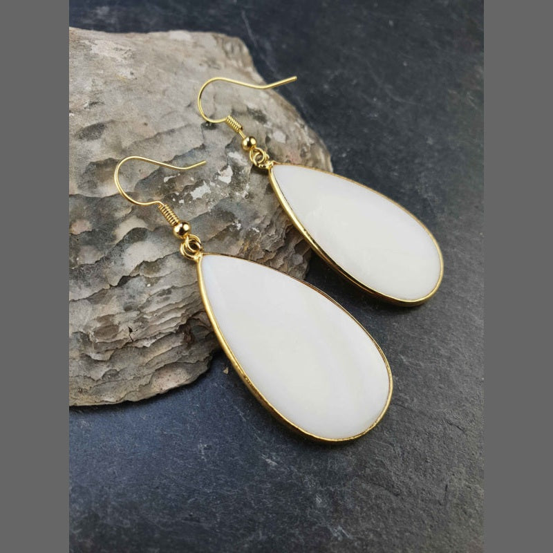 Witte parelmoeren oorbellen met goud edelstaal liggend tegen schelp | Big Taerdrop White Shell Gold