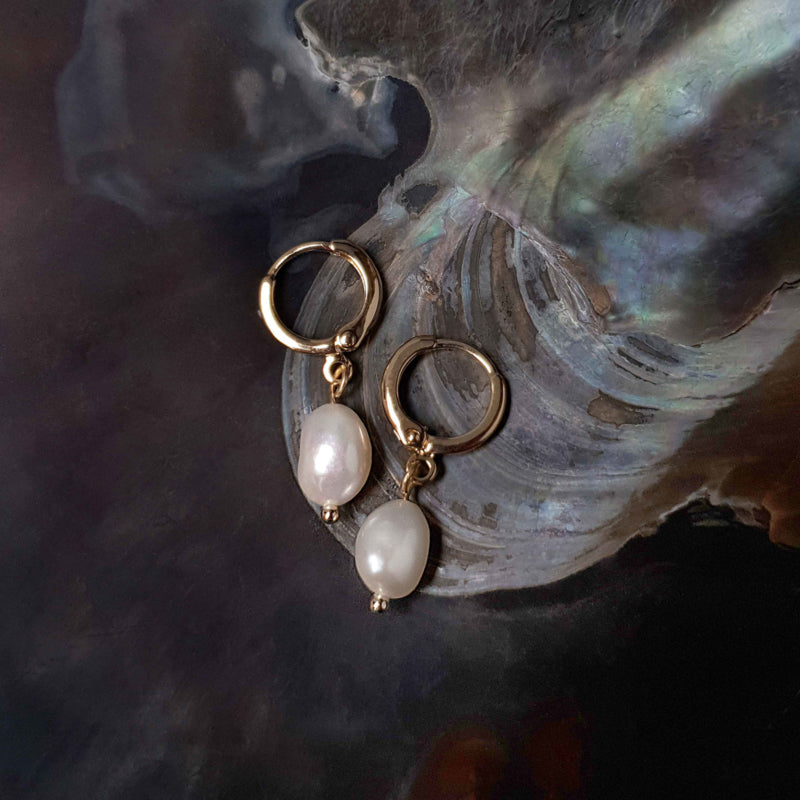 Witte zoetwater parel oorbellen met gouden edelstalen oorringen liggend in schelp | Cilia